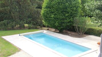Une piscine rectangulaire, dotée d’un bord lisse et de couleur claire, entourée d’une pelouse bien entretenue et de différents arbres.