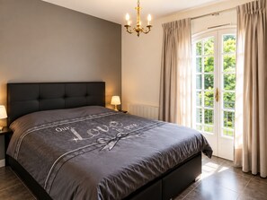 Une chambre à coucher avec un grand lit, un lustre, une table de chevet et une fenêtre avec des rideaux.