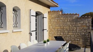 Une terrasse avec une table et des chaises, un mur en pierre et une porte avec des volets.