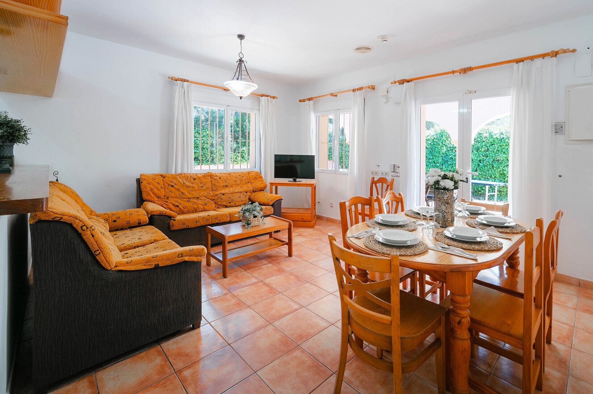 A living room with a sofa, TV, and dining area with chairs and a table set for four.