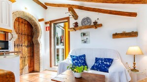Un salon chaleureux avec une porte en bois, un canapé blanc orné de coussins à motifs floraux bleus, une petite table avec une plante et une lampe.