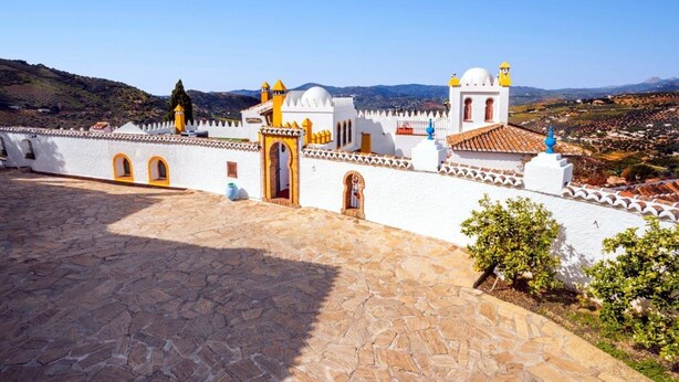 Un bâtiment blanc agrémenté de touches de jaune et doté d’une cour pavée de pierres.