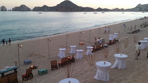 A beachside restaurant with round tables and chairs, set against a backdrop of calm sea and distant mountains. - Stunning Villa at Villa La Estancia, Directly on Medano Bay- Beautiful Views (Cabo San Lucas)
