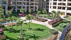 A multi-story hotel with balconies, a central courtyard with palm trees and flower beds, and a well-maintained lawn. - Stunning Villa at Villa La Estancia, Directly on Medano Bay- Beautiful Views (Cabo San Lucas)
