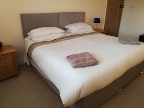 Cama bem arrumada com toalha dobrada, abajur e mesa de cabeceira de madeira.