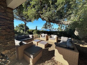 Zona esterna con sedute in vimini e cuscini, circondata da mura in pietra e alberi, con vista panoramica.
