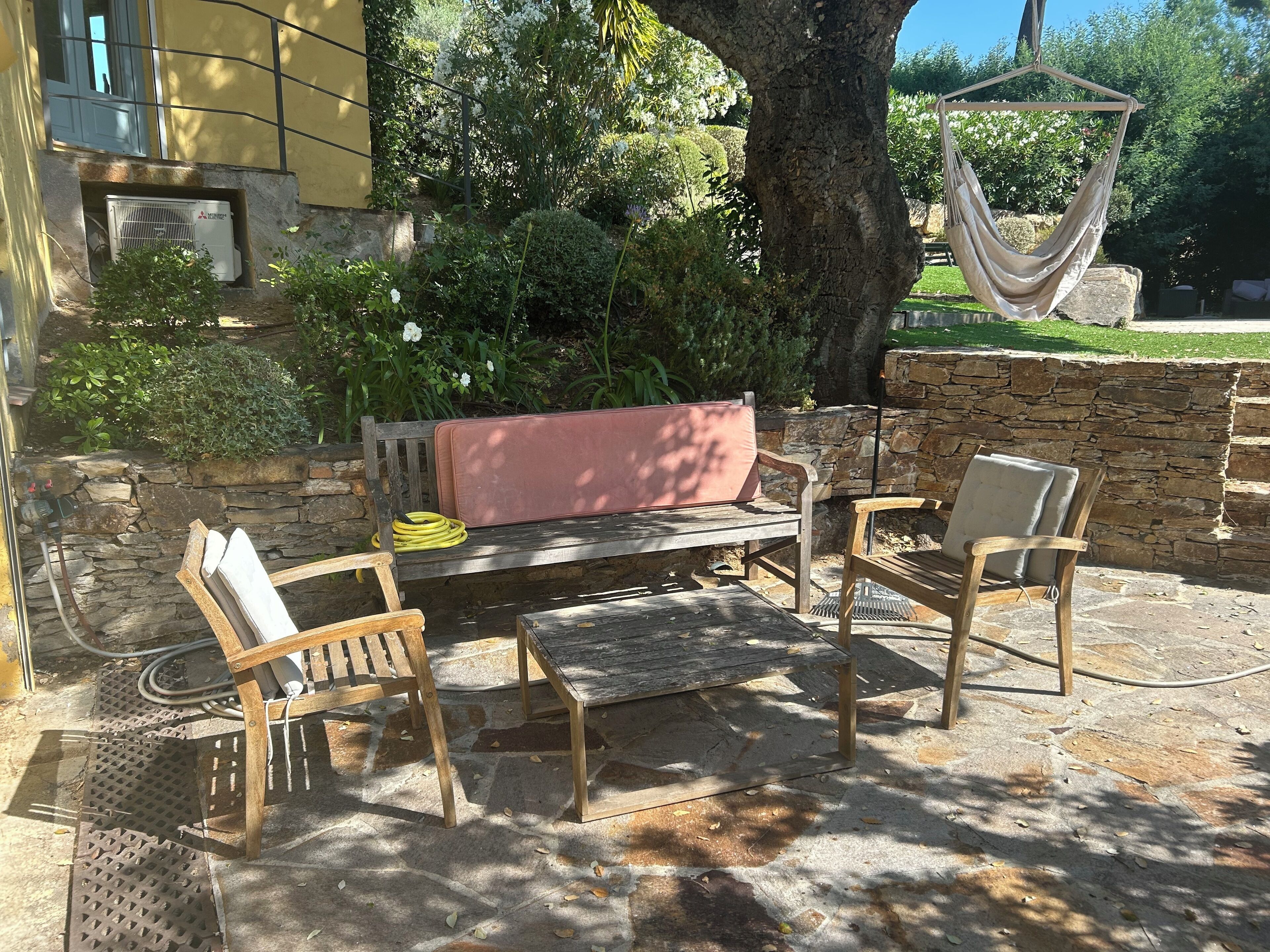 An outdoor seating area with a stone wall, a hammock, and a bench with a pink cushion.