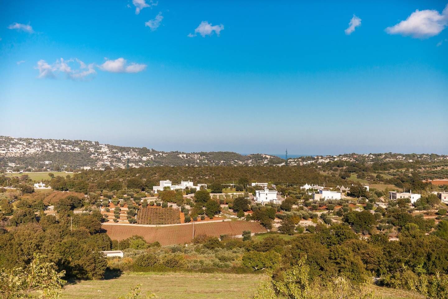 A coastal town with white buildings, green hills, and a clear blue sky.