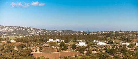 A coastal town with white buildings, green hills, and a clear blue sky.