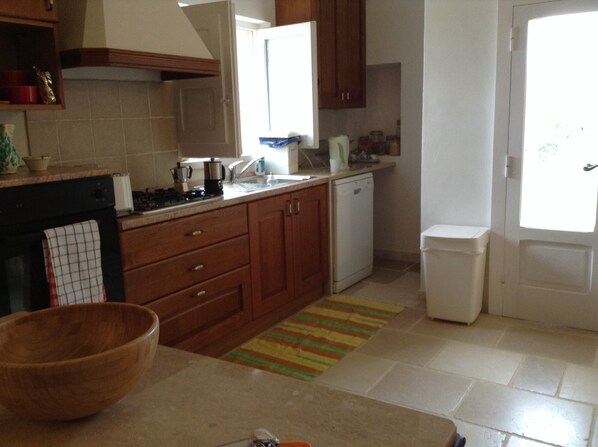 A kitchen with wooden cabinets, a stove, a sink, and a trash bin. - On top of a hill, in the heart of a village (Puglia)