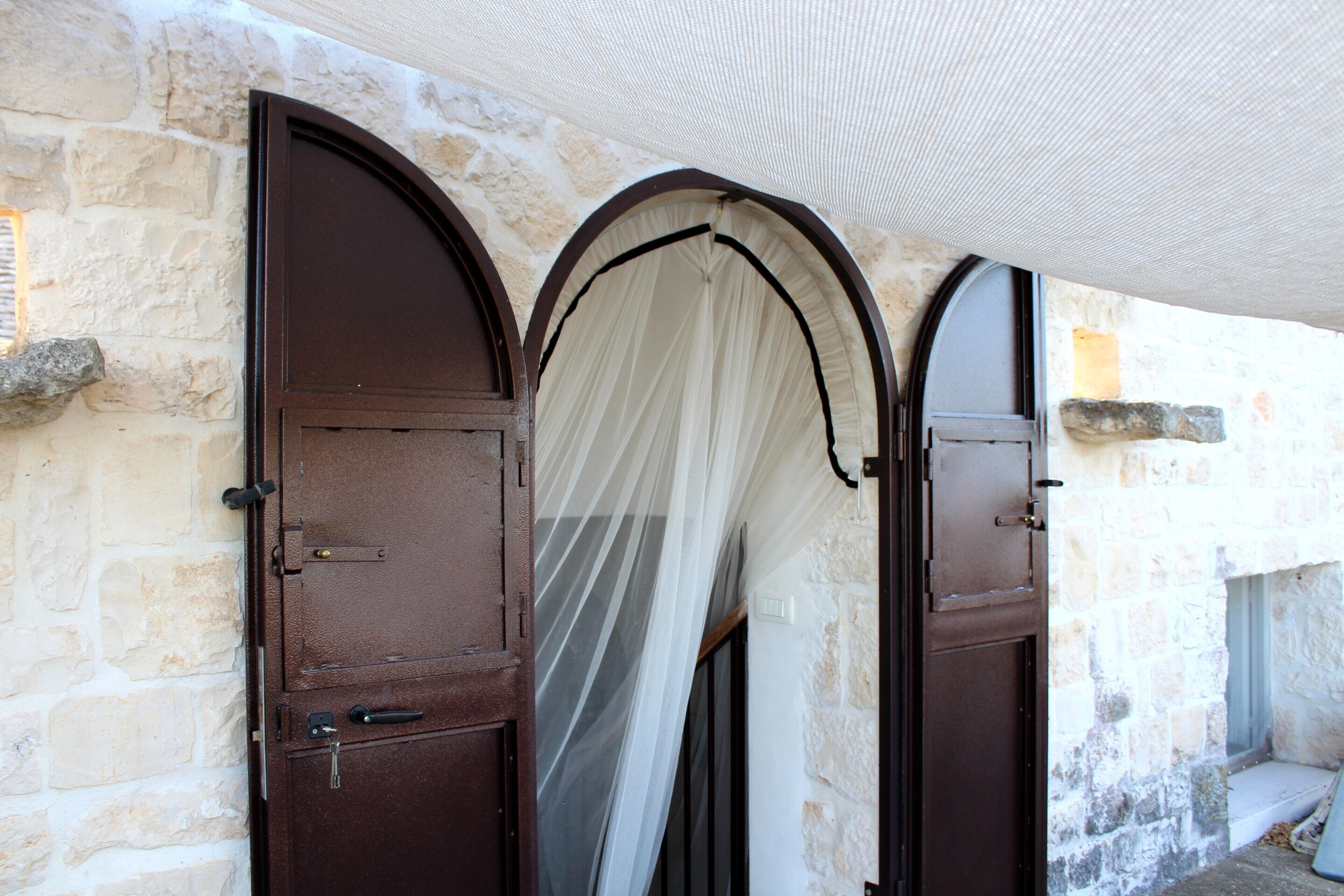 Ein Steinhaus mit drei Rundbogentüren, eine davon mit einem weißen Vorhang.