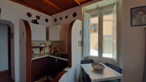 A compact kitchen with white cabinets, a stove, and a window overlooking a brick building.
