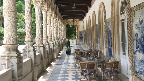 A covered corridor with ornate columns, checkered flooring, and wicker furniture. - Stylish accommodation with stunning views, private pool, vineyard (Penela, Coimbra)