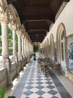 Un couloir couvert, orné de colonnes décoratives, doté d'un sol à carreaux et de meubles en osier.