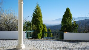 A cobblestone patio with a white column and green metal railing, overlooking a mountainous landscape. - Stylish accommodation with stunning views, private pool, vineyard (Penela, Coimbra)