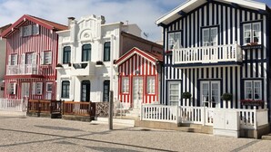 A row of colorful buildings with distinct architectural styles, including a white building with a red roof, a red and white striped building, and a blue and white striped building. - Stylish accommodation with stunning views, private pool, vineyard (Penela, Coimbra)