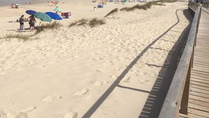 A sandy beach with a wooden boardwalk, beach umbrellas, and people enjoying the area. - Stylish accommodation with stunning views, private pool, vineyard (Penela, Coimbra)