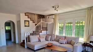 A spacious living room with a beige sofa, a wooden coffee table, and a clear glass chair. A staircase with wooden railings leads to an upper floor. - P2131- FANTASTIC VIEWS, AIR CONDITIONING, POOL AND WIFI (Sant Feliu de Guixols)