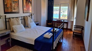 A bedroom with a bed, a nightstand, a desk, and a chair. There are two paintings on the wall, a window with a view, and a curtain. - P2131- FANTASTIC VIEWS, AIR CONDITIONING, POOL AND WIFI (Sant Feliu de Guixols)