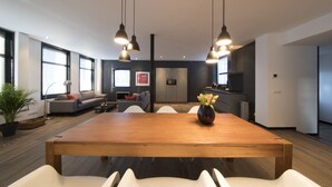 A modern living space with a wooden dining table, white chairs, a sofa, and a kitchen area. - Villa Antonius Amsterdam (Ouderkerk aan de Amstel)