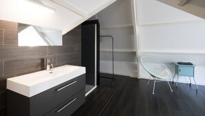 A modern bathroom with a white vanity, dark wood flooring, a large mirror, and a white chair. - Villa Antonius Amsterdam (Ouderkerk aan de Amstel)