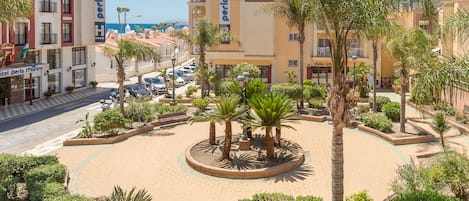 A hotel with a central courtyard surrounded by palm trees and a sandy area, with a view of the sea in the background.
