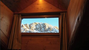 Een houten hutje met een raam dat uitkijkt op een besneeuwde berg.