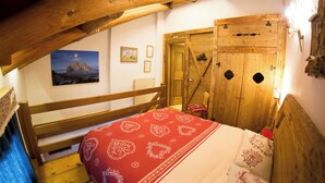 Een slaapkamer met een houten bed, een rood bed met een dessin, een houten deur en een lijst met een afbeelding aan de muur.