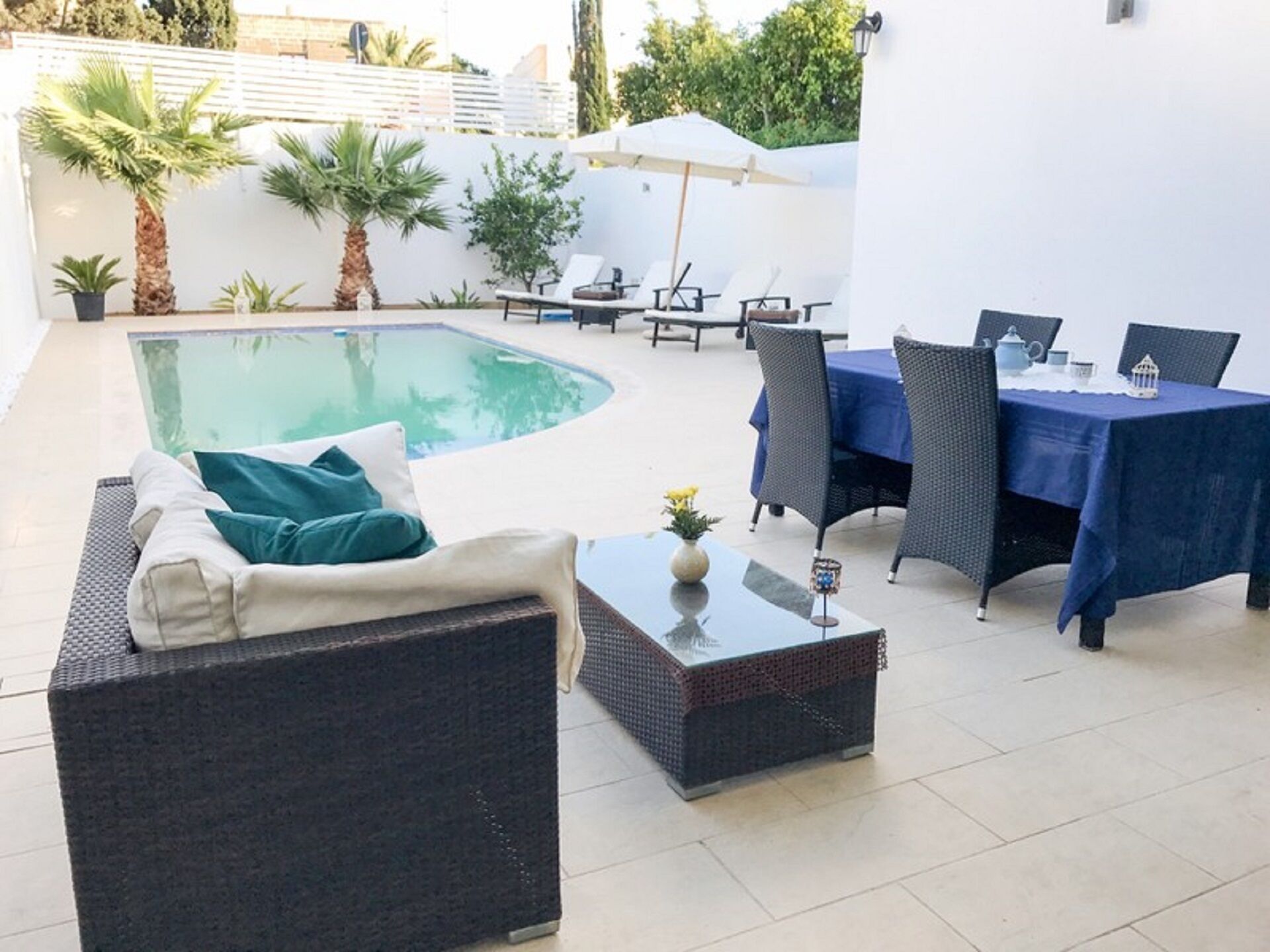 Een zwembadterras met een bank, stoelen en een tafel.