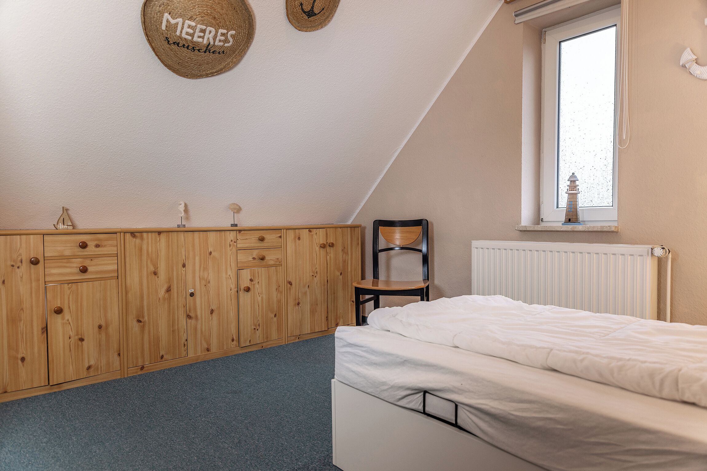 A bedroom with a bed, wooden wardrobe, chair, and a window with a view.