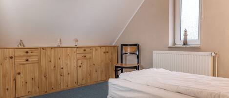 A bedroom with a bed, wooden wardrobe, chair, and a window with a view.