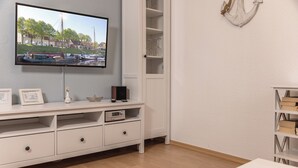 Huoneessa on seinälle asennettu televisio, valkoinen lipasto laatikoineen ja kirjahylly.