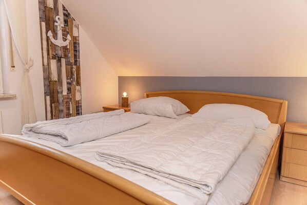 A neatly made bed with white bedding, a wooden headboard, a nightstand with a lamp, and a wall with a wooden plank pattern. - Simply relax and enjoy the fresh North Sea air: (Carolinensiel)