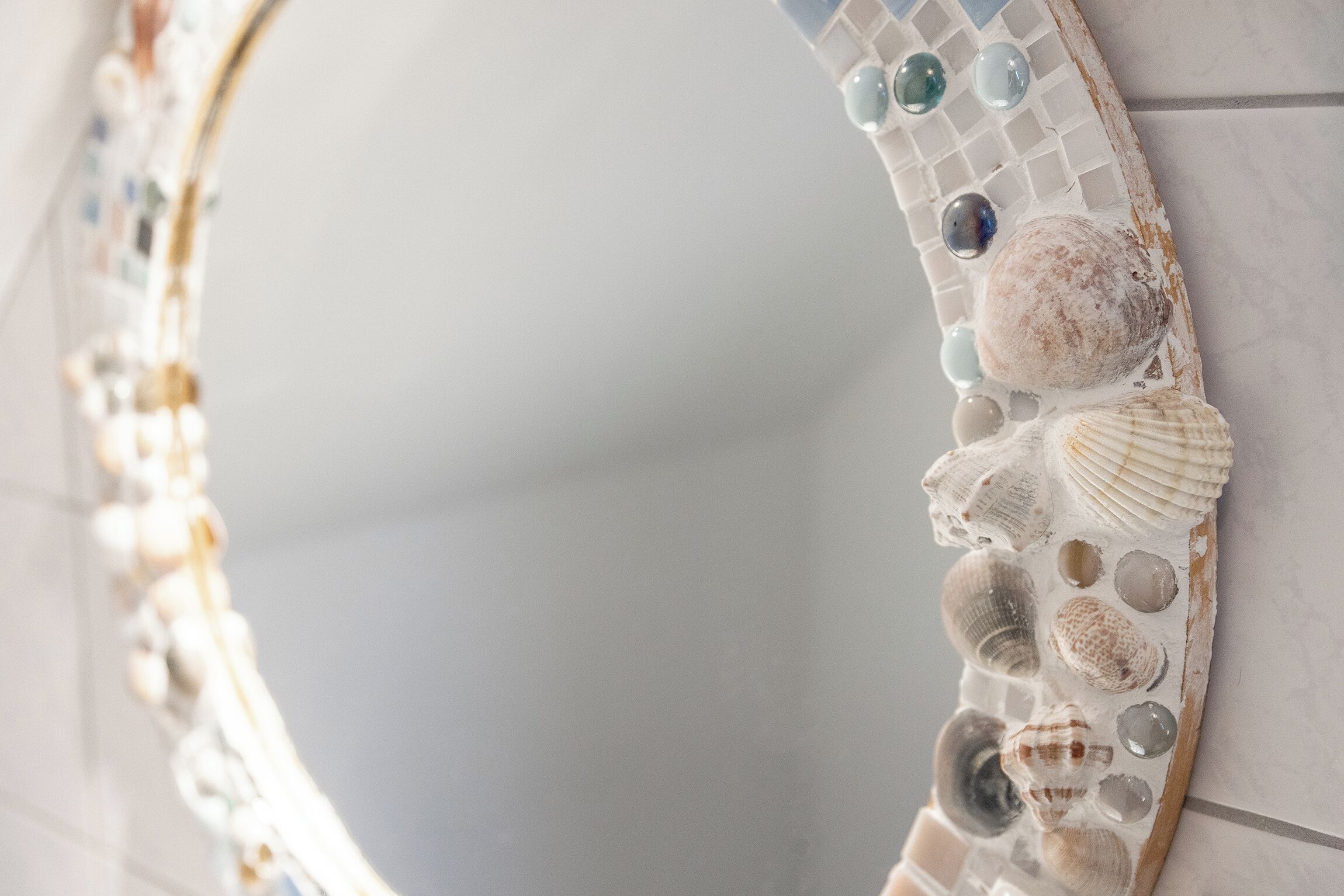 A mirror with a mosaic border featuring seashells and glass pieces.