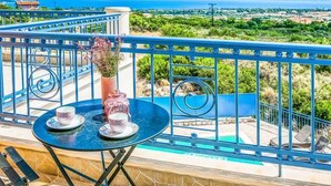 A balcony with a table set for two, overlooking a pool and a scenic landscape. - Villa Xenia (Kefalonia)