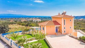 A two-story building with a red-tiled roof, a small porch, and a view of the sea and distant landscape. - Villa Xenia (Kefalonia)