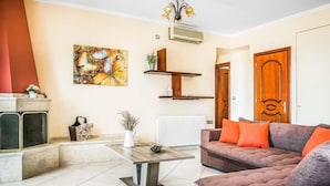A living room with a sofa, a coffee table, a fireplace, a radiator, and a wall-mounted shelf. - Villa Xenia (Kefalonia)