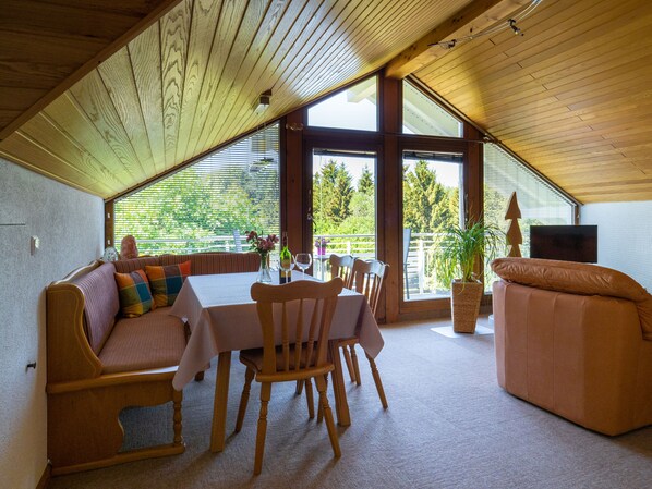 Un interior acogedor con techo de madera, una mesa de comedor con sillas, un sofá y un televisor.