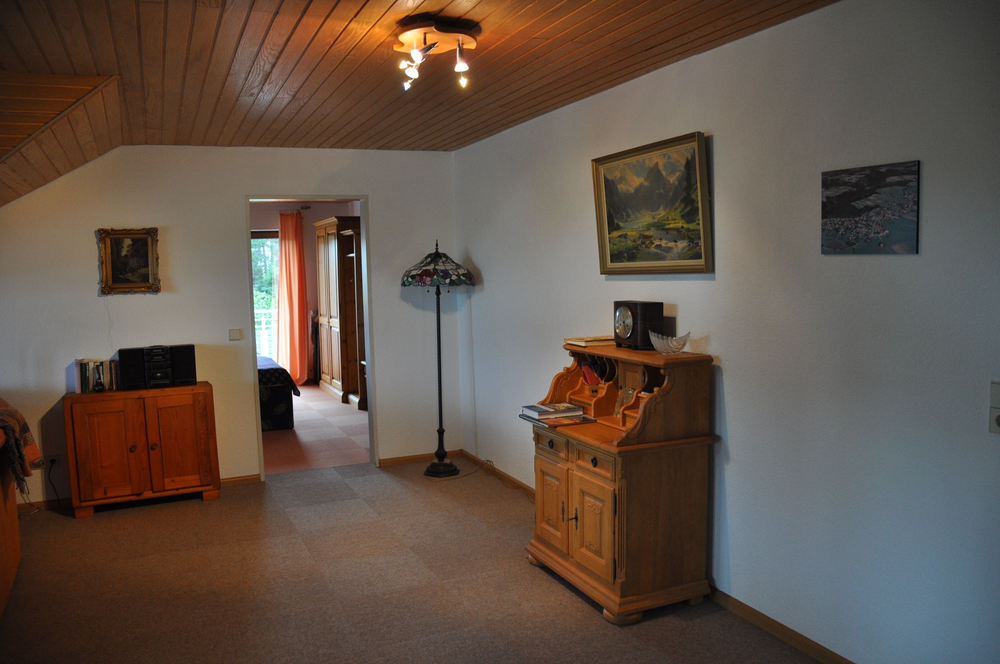 A spacious room with a high ceiling, wooden cabinets, a floor lamp, and artwork on the walls.