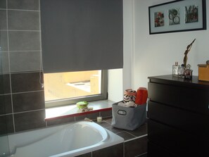 Une salle de bain avec une baignoire, une fenêtre donnant sur un beau paysage, un meuble-lavabo avec des articles de toilette et un tableau encadré au mur.