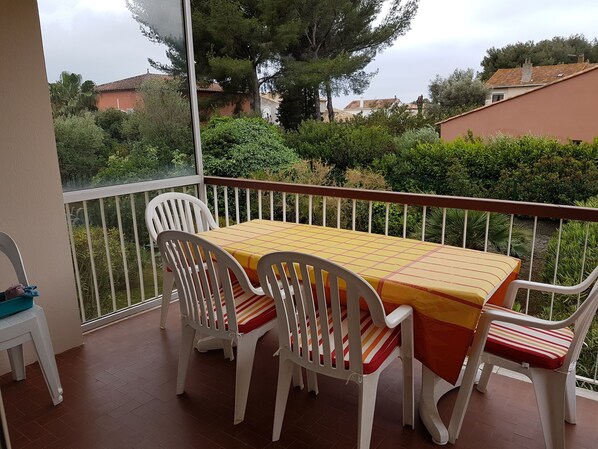 Een balkon met een tafel en stoelen, uitzicht op groen en gebouwen, en een leuning.