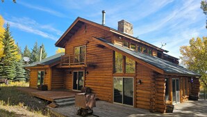 A log cabin with a balcony, large windows, and a chimney.