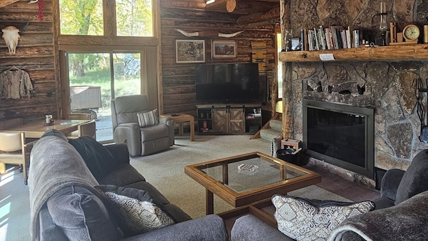 A rustic cabin interior with a stone fireplace, wooden furniture, and a large window.