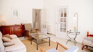 Un salon comprenant un canapé, une table basse avec un plateau en verre, un fauteuil à motifs, un meuble en bois et un lampadaire.