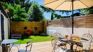 Une terrasse extérieure dotée d’une plateforme en bois, de chaises en métal, d’une table recouverte d’une nappe blanche et d’un grand parasol.