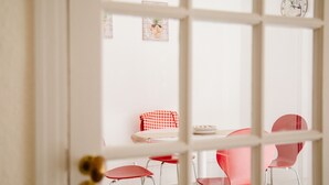 Un coin repas avec une table et quatre chaises rouges, une nappe à carreaux et une horloge murale.