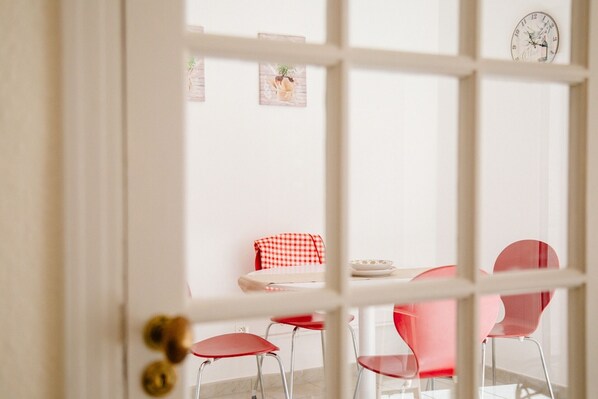 A dining area with a table and four red chairs, a checkered tablecloth, and a wall clock.