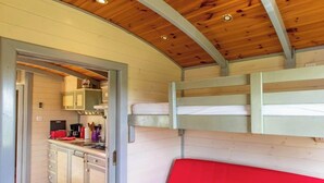 Une cuisine compacte, dotée de placards et d’une cuisinière, d’un banc rouge et d’un plafond en bois.