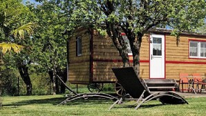 Une cabane en bois avec une véranda, des sièges d’extérieur et une petite brouette.
