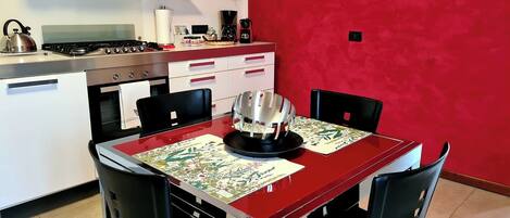 Una cocina con una pared roja, una mesa de comedor con sillas y una cafetera.